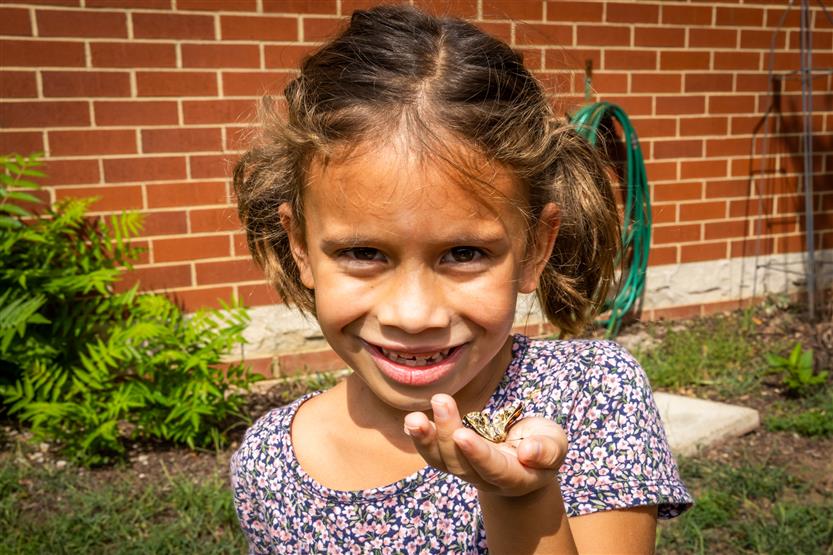 A girl holds up a butterfly and smiles